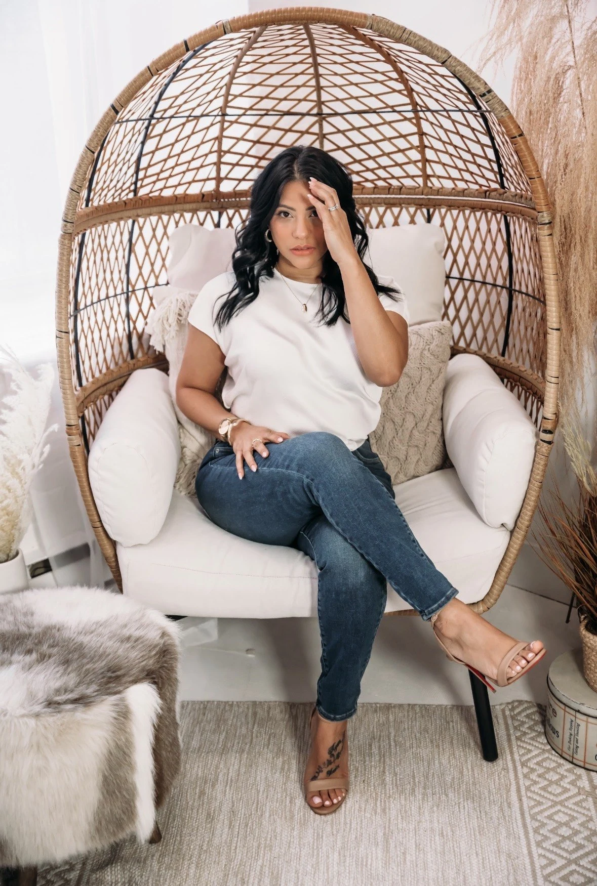Shay seated in a woven chair wearing white and jeans